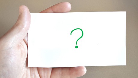 En person håller i ett vitt kort med ett grönt frågetecken på.
